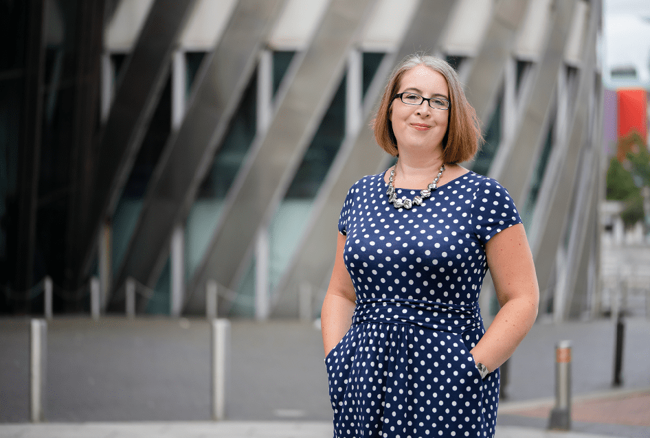 Hannah Paskin in a blue polka dot dress standing in front of a building offering OCD therapy.