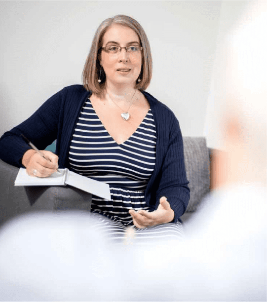 Hannah Paskin sitting on a couch talking to her client as a therapist.