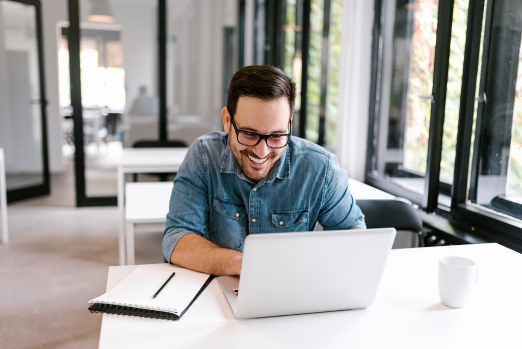 A stock photo of a male sat in front of his laptop at a desk, engaging in a video OCD therapy session, with a notepad at the side.