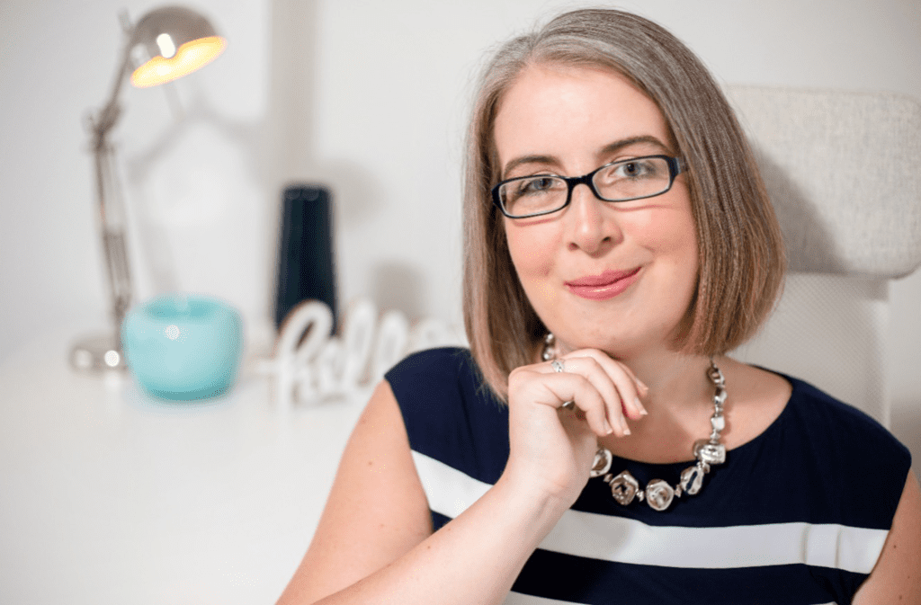 Hannah Paskin - wearing glasses, sitting at a desk.