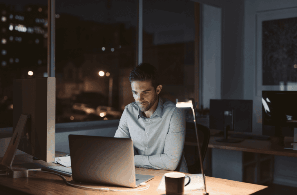 A man working late at night on his laptop in a well-lit office.