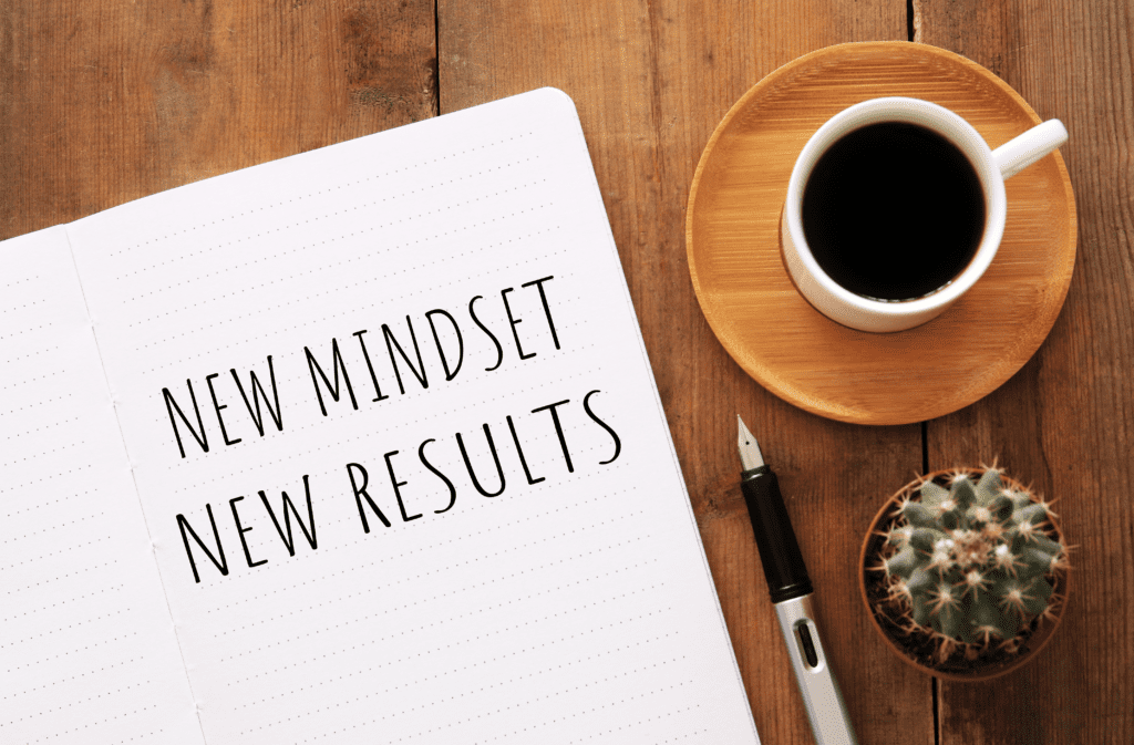 The image shows a notepad and a cup of coffee on a desk. The notepad says new mindset new results