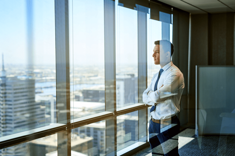 A burnt-out businessman standing in front of a window in an office.
