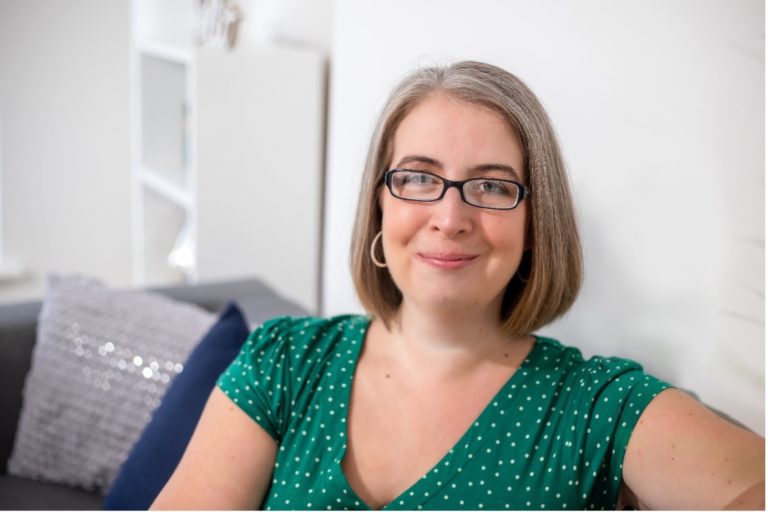 A photograph of me, Hannah Paskin looking relaxed in my therapy room. I'm wearing a green spotty dress.