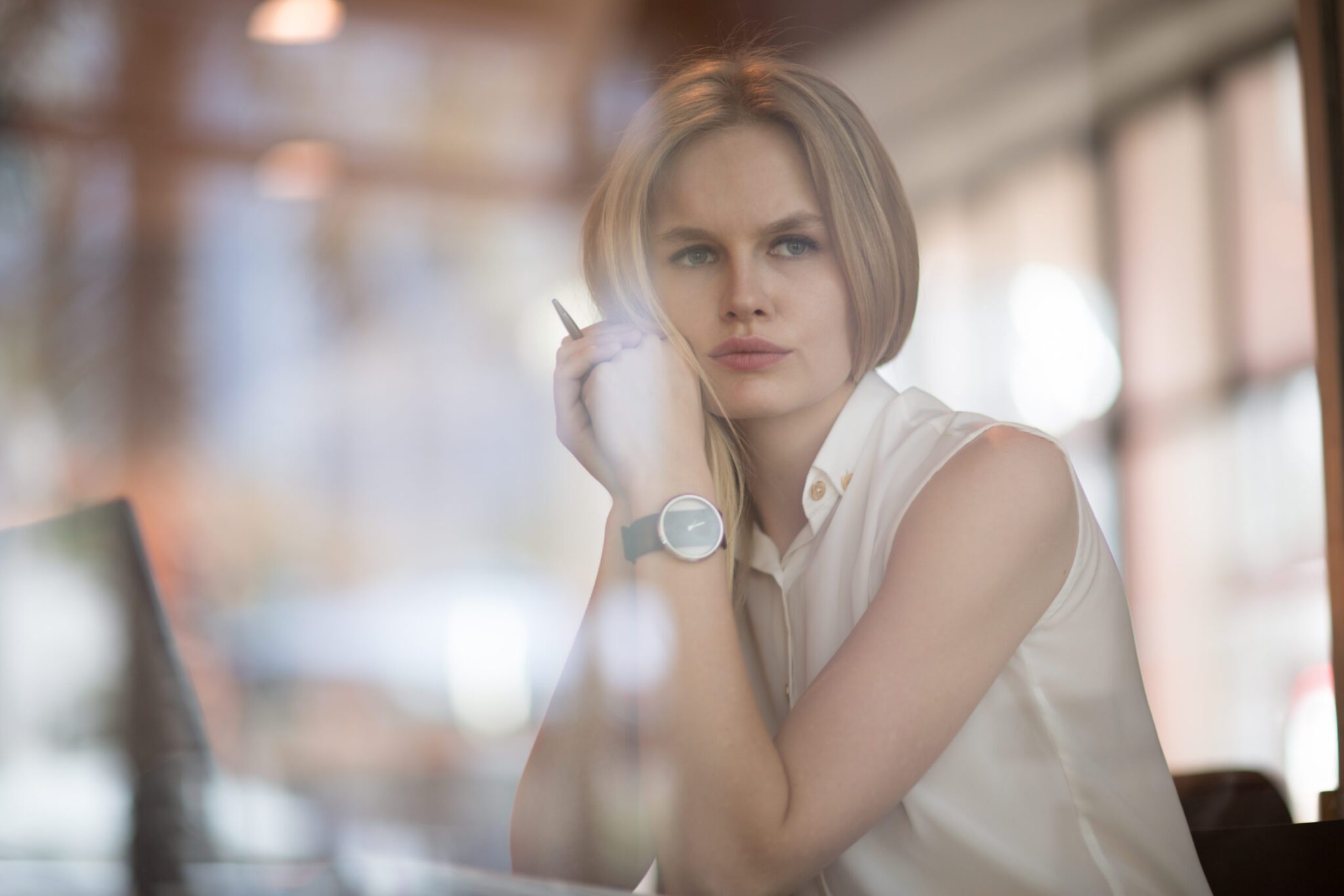 A stock photo through the glass of a woman at work looking contemplative. Women experience imposter syndrome just as much if not more than men.