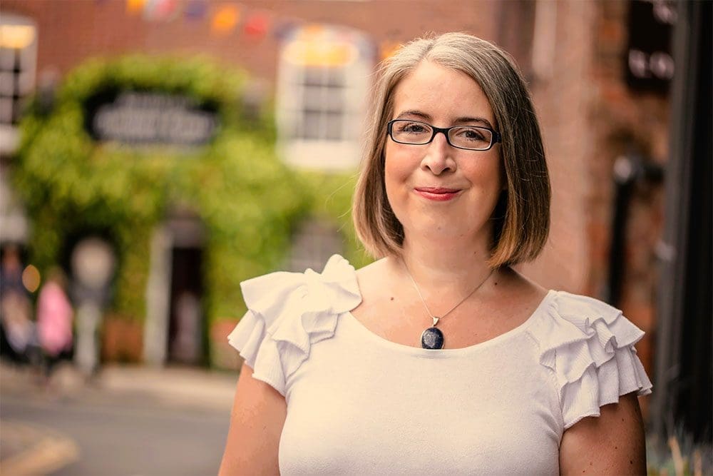 Hannah Paskin Counsellor. She is shown in a professional photograph that was taken in Knutsford Cheshire. She wears a white top with a necklace and earrings. She has pale bob cut hair and smiles at the camera