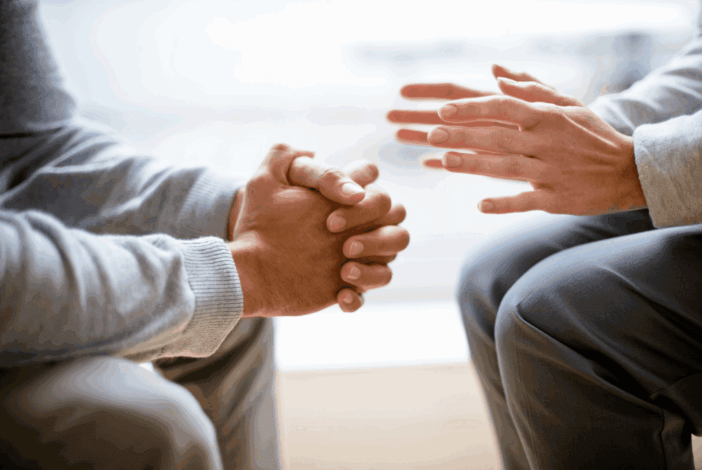 Photo is zoomed in on 2 hands. One person clasps their hands, the other's hands are more open.