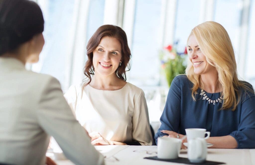 Three professional women engaged in a conversation over coffee.