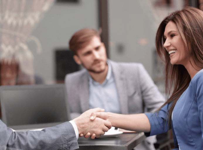 A smiling woman engaging in a business discussion with a handshake.