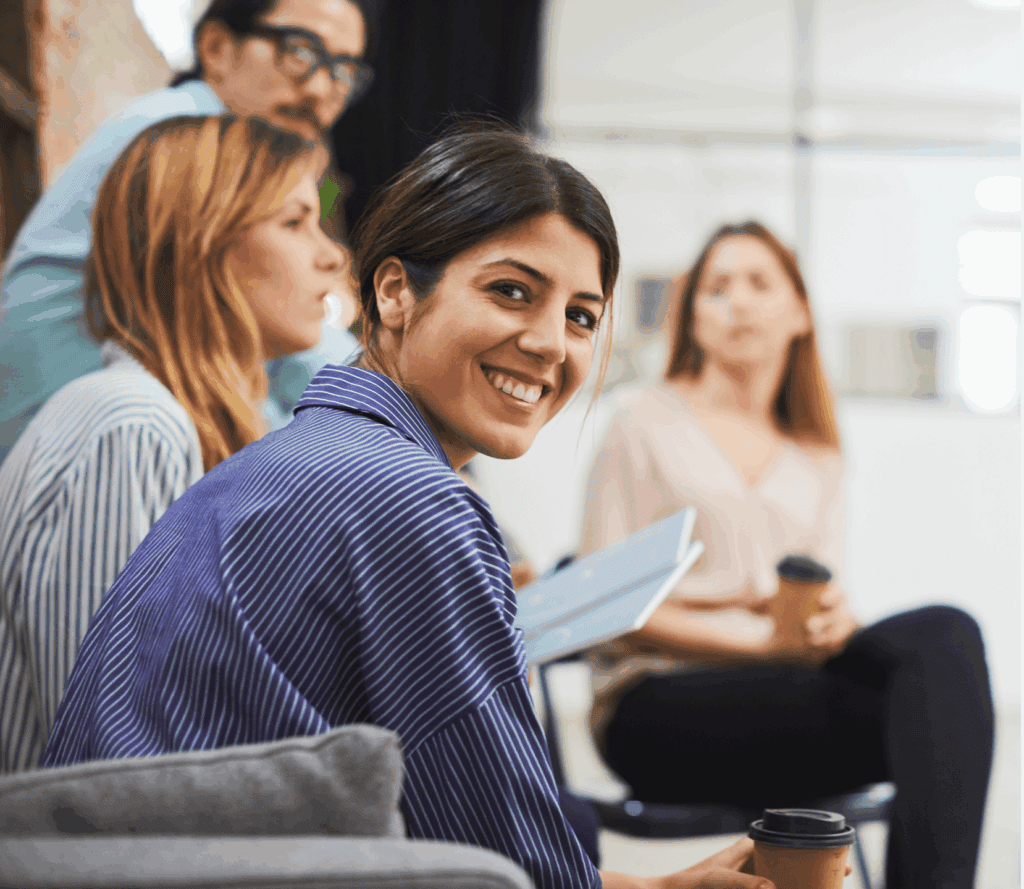 A smiling woman in a meeting with colleagues, holding a coffee cup.