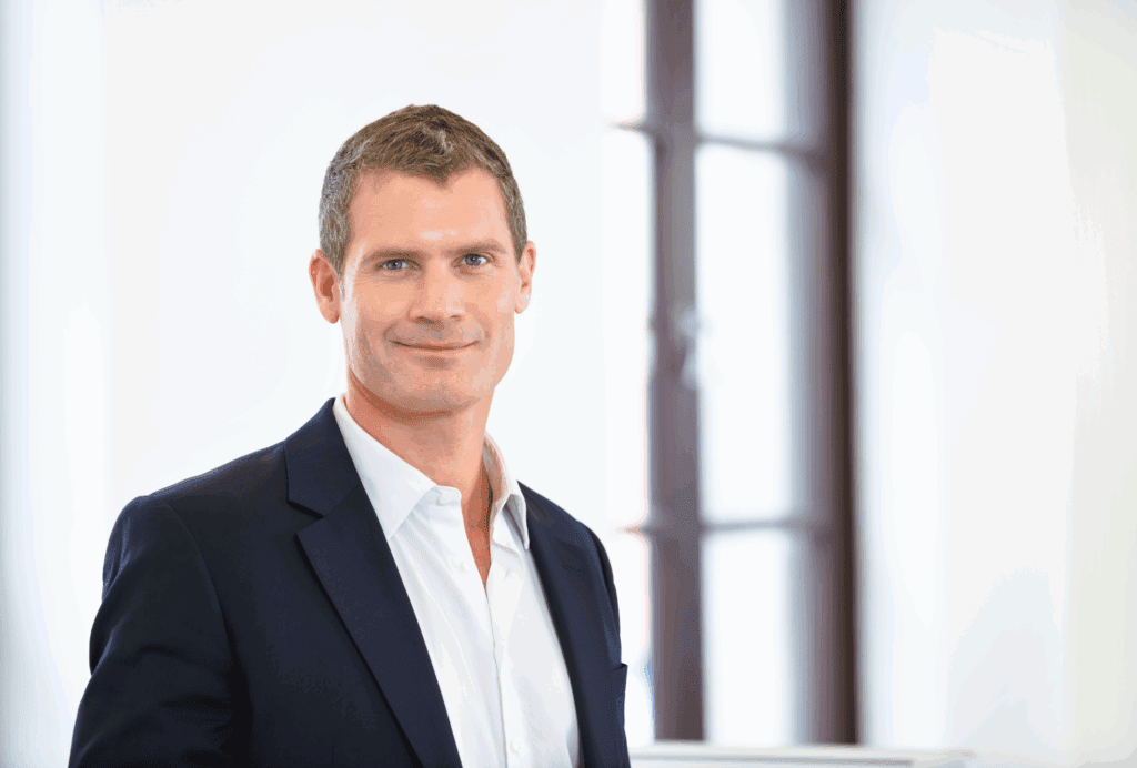 A stock image. The photo shows a males head and shoulders. He has mid brown hair. He wears a white shirt open collared and a navy jacket. The background is white