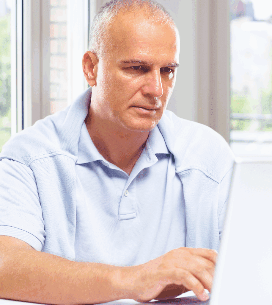 Image shows a couple that are male female. They are embracing. She is smiling, and he is kissing the top of her head. She faces the camera direction, he faces sides wards to her. They are stood in a field outside.