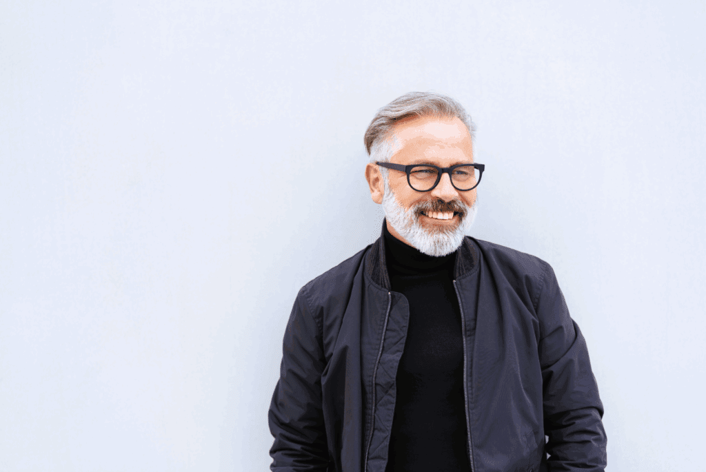 Young female in the street. She is paused outside a building to look at her phone. Her phone is in her hand. She wears a white tshirt and grey jacket. She has hoop earrings and dark curly hair.