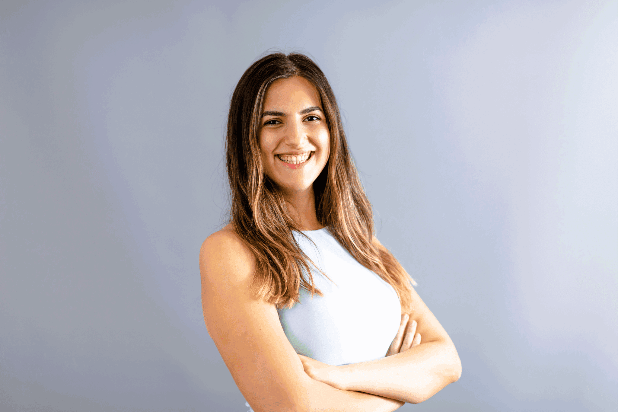 A female stood with arms crossed. She wears white and has dark wavy hair.