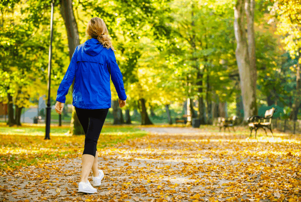 We see the back of a female as she walks. She's on a path between trees. She wears leggings trainers and a rain jacket. She has her hair tied backi