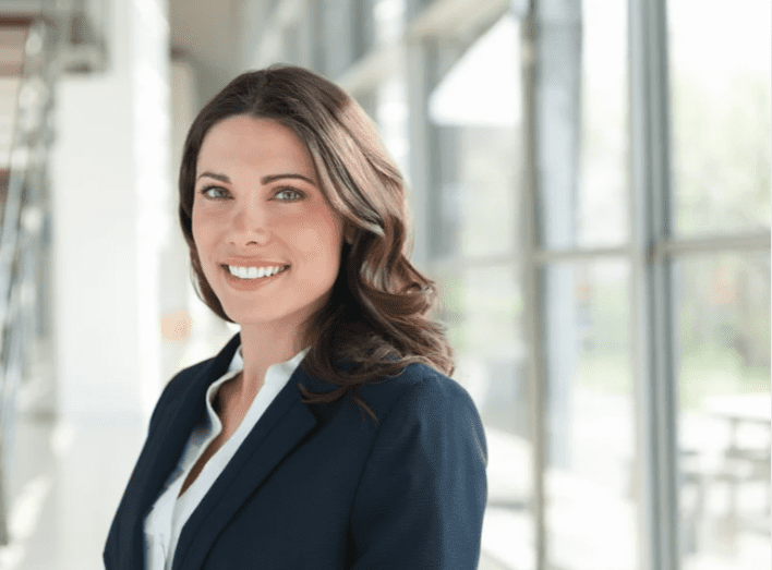 Woman in business attire standing confidently in a bright office.