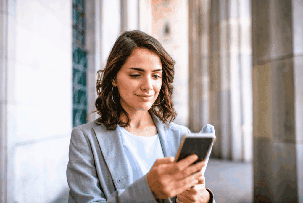 A woman in a grey blazer looking at her phone with a smile.