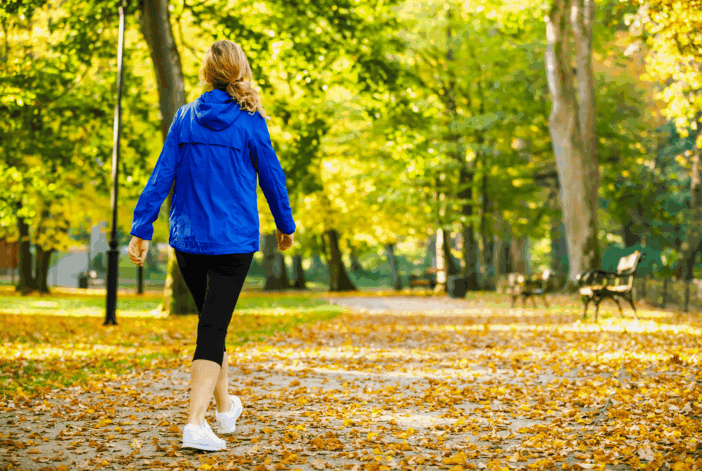 We see the back of a female as she walks. She's on a path between trees. She wears leggings trainers and a rain jacket. She has her hair tied backi