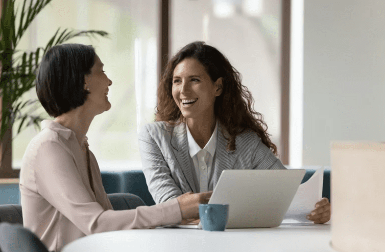 Women in a business meeting, smiling and working together with documents and a laptop.