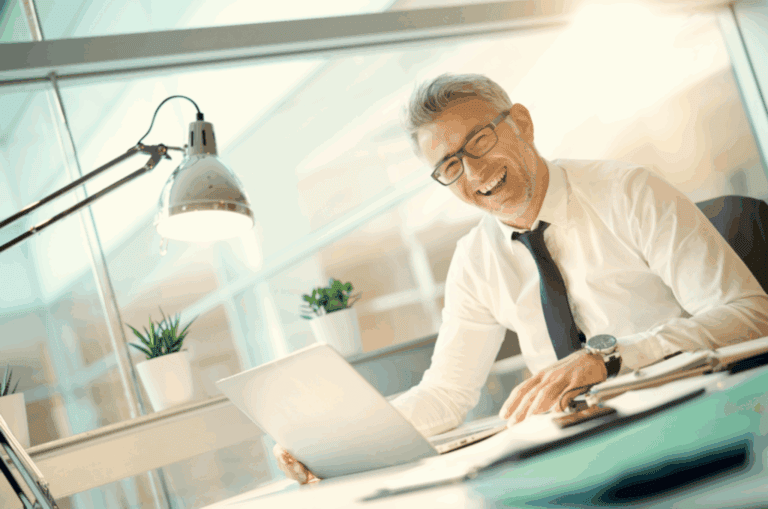 A smiling businessman working on a laptop in a bright office environment.