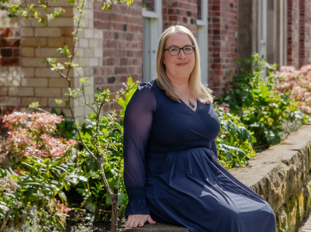 Hannah Paskin in a blue dress sitting in a garden with flowers and greenery.