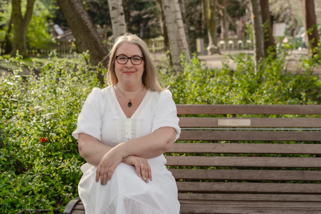 Hannah Paskin in a white dress sitting on a wooden bench in a garden.